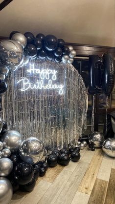 a happy birthday sign surrounded by balloons and streamers in a room with wood flooring