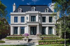 a large white house with lots of windows and bushes in front of the entrance to it