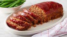 sliced meatloaf on a plate with green beans in the bowl next to it