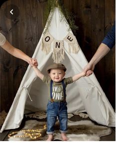 a little boy standing in front of a teepee with his hands up to him