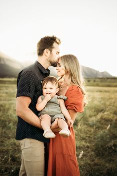 a man and woman holding a baby while standing in an open field