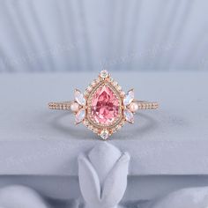 an engagement ring with a pink stone surrounded by white stones and diamonds on a light blue background