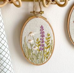 two embroidered flowers hanging from hooks on a wall