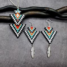 Embrace the rich essence of tribal and Southwestern style with this vibrant earrings and necklace set, featuring a creative double triangle design. The primary black and white colors are beautifully accented with turquoise, red, orange, and gold, adding a bold, captivating contrast. Delicate metallic feather charms enhance the boho and ethnic appeal, making this set perfect for any occasion. Crafted with intricate detail and creativity, this unique set is a statement piece for any jewelry collec Double Triangle, Boho Mode, Earrings And Necklace Set, Earrings Patterns, Beaded Earrings Patterns, Earrings And Necklace, Writing Gifts, Triangle Design, Feather Charms