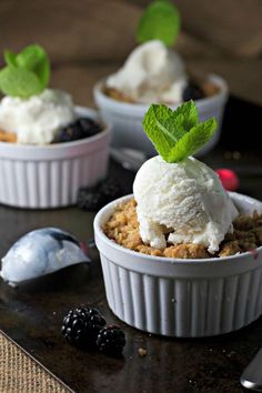 two small bowls filled with ice cream and blackberries on a table next to a spoon