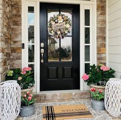 a black front door with two white wicker chairs and pink flowers on the side