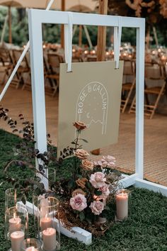 an outdoor ceremony with candles and flowers on the grass in front of a sign that says,