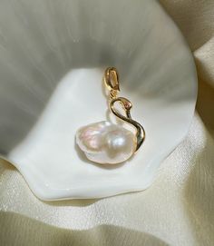 Capture the grace of a swan with our Gold / Silver Swan Pearl Necklace, a symbol of purity and refinement. This stunning piece features a lustrous natural pearl gracefully set in a golden swan design, perfect for elevating any outfit from ordinary to extraordinary. Comes with necklace chain. Available in regular or premium quality pearls. Measurements: Pearl Size:  around 14*20mm  (0.55'' * 0.78'') Pendant Size: around 23*25mm  (0.9'' * 1'') Necklace Length: 40cm  (15.7 '') Materials: AAA+ Fresh Swan Necklace Aesthetic, Ocean-inspired Gold Shell With Pearl Pendant, Elegant Gold Shell-shaped Pearl Necklace, Swan Locket, Swan Pendant Gold, Swan Design, Swan Jewelry, Gold Swan, Swan Pendant