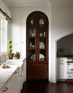 a kitchen with white cabinets and wood flooring next to a large glass doored cabinet