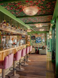 the bar is decorated with floral wallpaper and pink stools, along with green walls