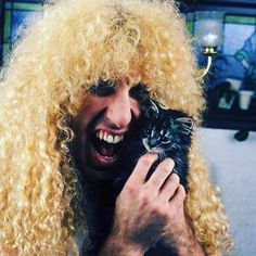 a man with long blonde hair holding a cat in his hands and smiling at the camera