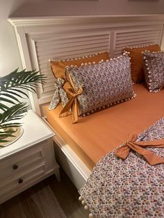 a bed with pillows and bows on the headboard, next to a potted plant