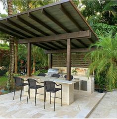 an outdoor kitchen with grill and chairs under a pergolated roof, surrounded by palm trees