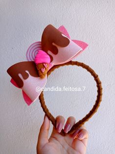 a hand is holding up a pink and brown hair bow on a headband that has an ice cream cone in the shape of a heart