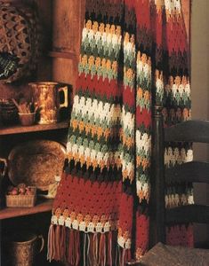 a crocheted blanket is hanging on a chair next to a table and bookshelf