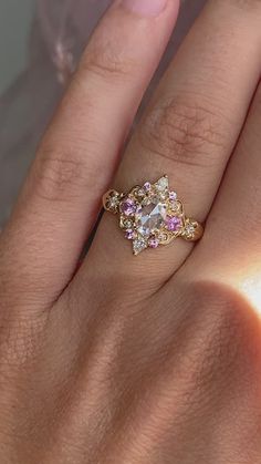 a woman's hand with a gold ring and pink stones on the middle finger