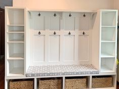 a white bench with baskets underneath it and several coat racks on the wall behind it