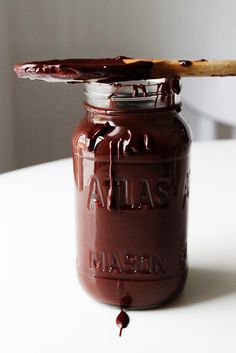 a jar of chocolate spread on top of a white table with a wooden spoon in it