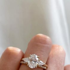 a woman's hand holding a three stone diamond ring with two pear shaped diamonds on it