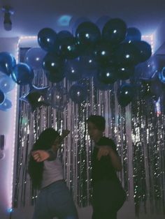 two people dancing in front of balloons and streamers on the wall with lights behind them