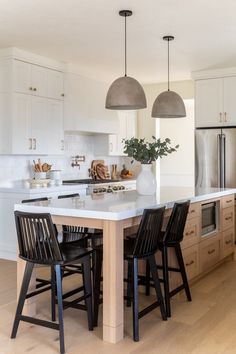 a kitchen with white cabinets and black chairs next to an island in the middle of the room