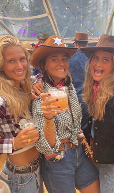 three women in cowboy outfits holding drinks and smiling at the camera while standing next to each other