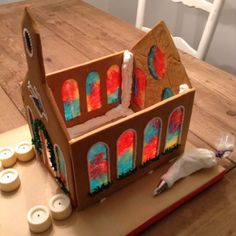 a cardboard doll house sitting on top of a wooden table next to candles and other items