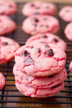 chocolate chip cookies with red and pink icing are arranged on a baking sheet, ready to be eaten