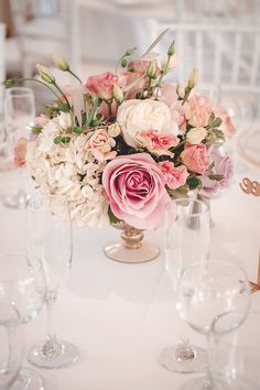 a vase filled with pink and white flowers on top of a table next to wine glasses