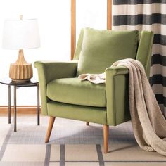 a green chair sitting in front of a window next to a table with a lamp on it