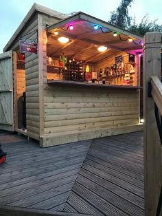 a small wooden bar on a deck with lights hanging from it's roof top