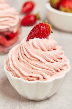 a strawberry cupcake with whipped cream and strawberries in the background