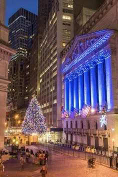 a christmas tree is lit up in the middle of a city square with tall buildings