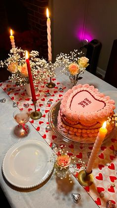 a heart shaped cake sitting on top of a table next to two lit candles and flowers