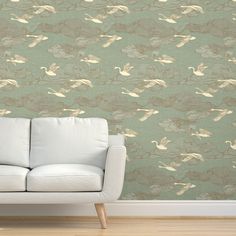 a white couch sitting in front of a green wallpaper with swans and clouds on it