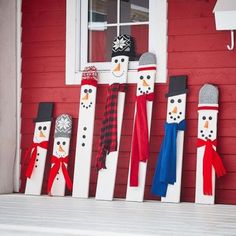 some snowmen are standing in front of a red house with scarfs on them