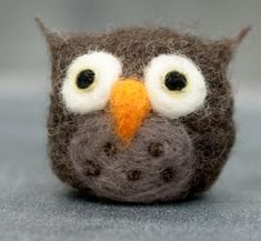 an owl made out of wool with eyes wide open sitting on a table next to a gray surface