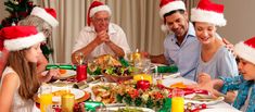 a group of people sitting around a table with christmas hats on their heads and plates in front of them