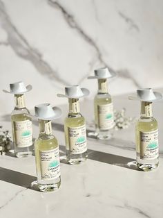 six bottles of hand sanitizers sitting on a marble counter with flowers in the background