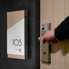 a person is opening a door with the number 103 on it and there is a wooden plaque mounted to the wall