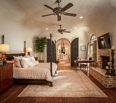 a bedroom with a bed, ceiling fan and fireplace in the middle of the room