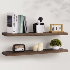 two wooden shelves with books, candles and other decorative items on them against a white wall