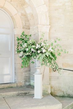 a tall white vase filled with flowers sitting on top of a stone step next to a doorway