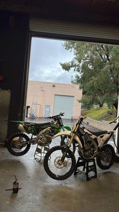 two dirt bikes parked next to each other in front of a garage door with an open window