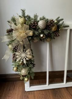 a wreath with pine cones and ornaments hanging on the wall next to a white frame