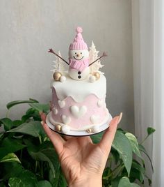 a hand holding a cake with a snowman on top