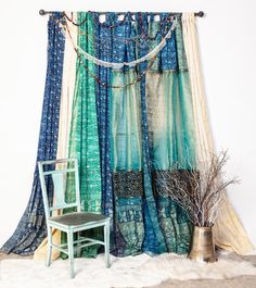 a chair sitting next to a window covered in blue and green curtain panels with string lights