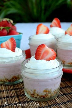 small desserts with strawberries and whipped cream in glass jars on a bamboo mat