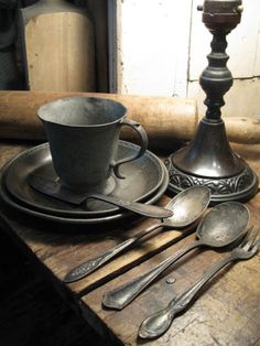 an old wooden table with silverware and spoons on it, next to a candle holder