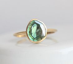 an oval shaped green tourmaline gemstone sits on a gold band, set in a bezel setting